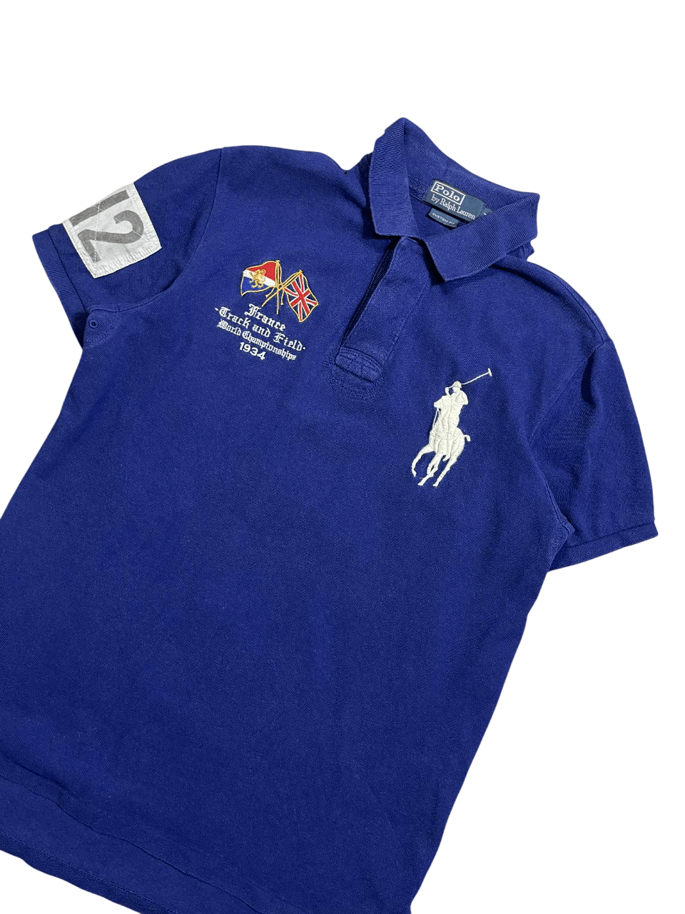 Kék vintage Ralph Lauren póló, hímzett logóval és zászlókkal, sportos streetwear stílus