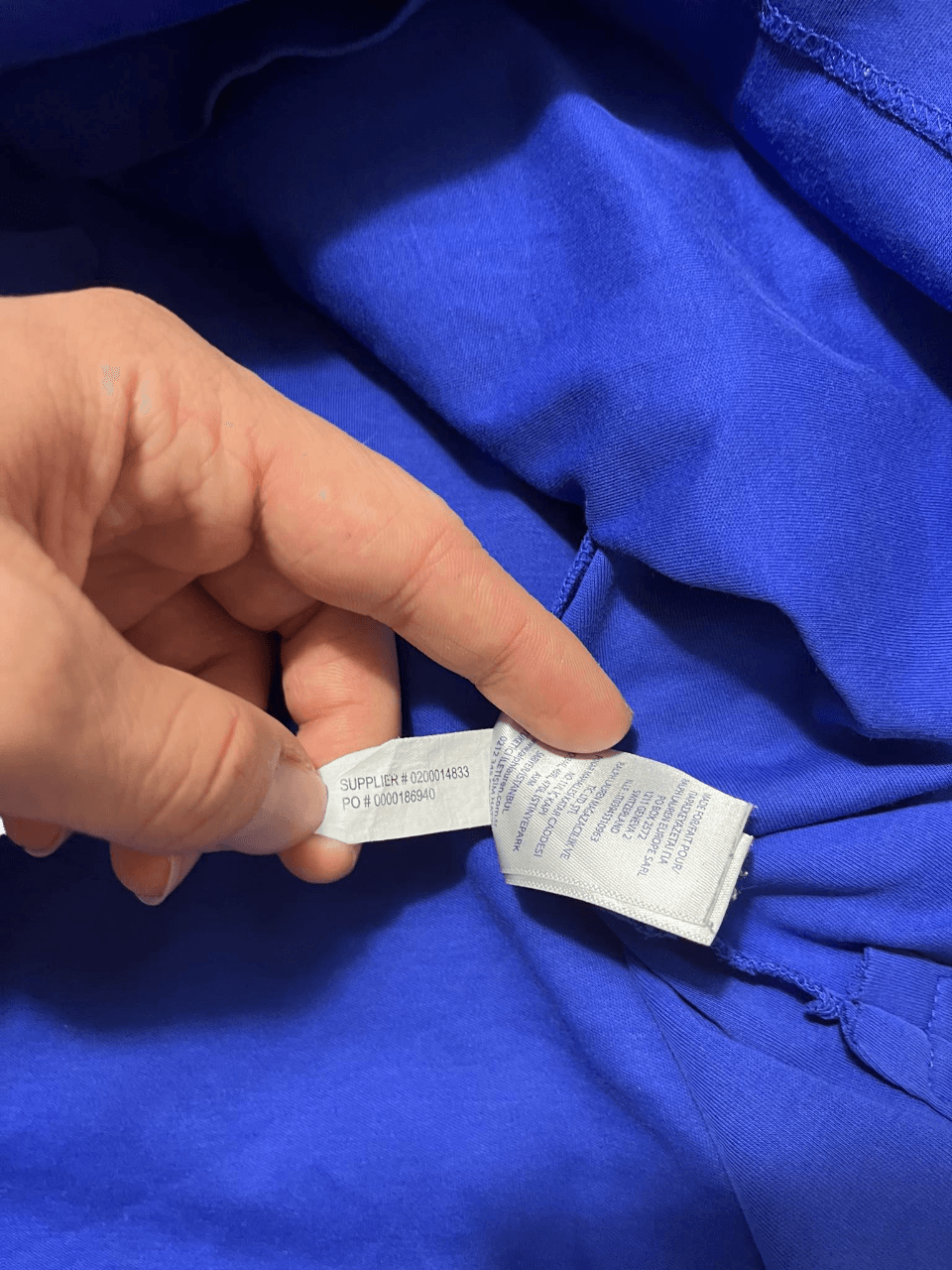 Kéz által tartott, kék streetwear felső címkéje, felirattal, közelről