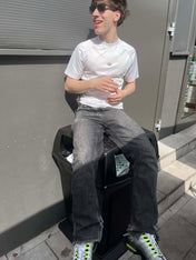 Fiatal férfi napszemüvegben, fehér streetwear pólóban, szürke farmerben és sportcipőben ül kint