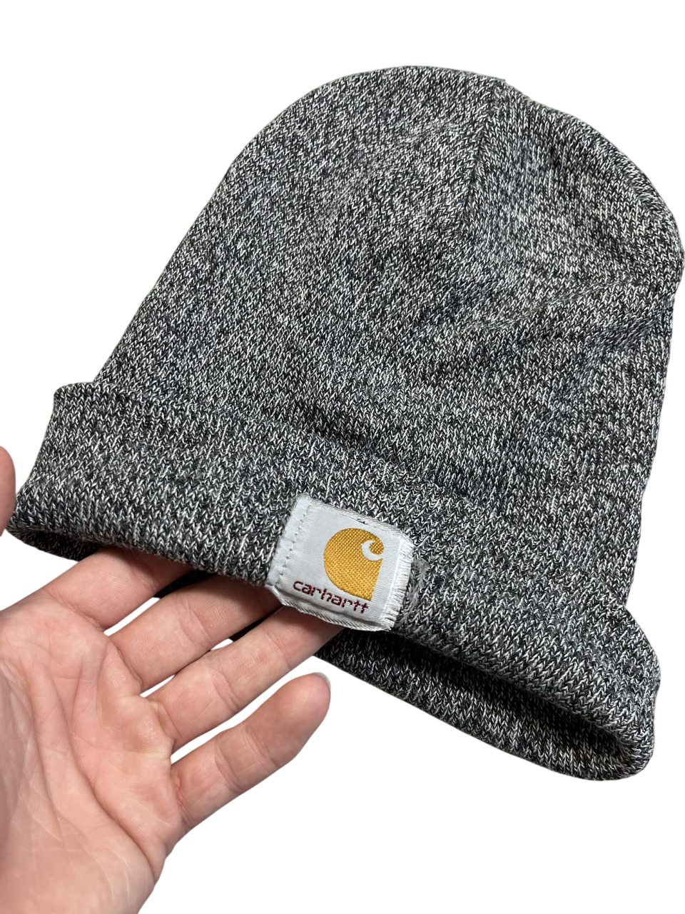 Szürke Carhartt kötött sapka kézben, streetwear stílus, márkajelzéssel az elején.